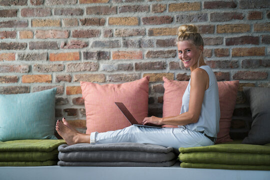 Mature woman sitting on couch, usine laptop