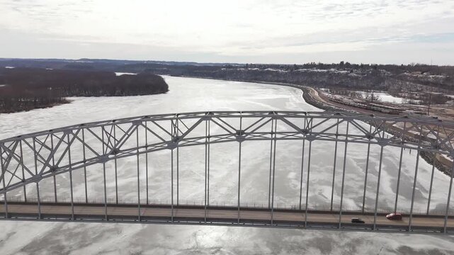 Establishing drone shot of a winter bridge scene in Dubuque, Iowa featuring frozen water, light traffic, and surrounding urban development. Ideal for travel, documentary, or commercial use.