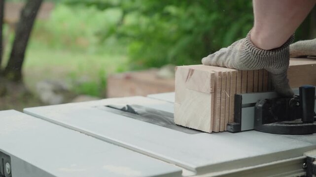 Close-up of gloved hands pushing stacked wood through table saw for precise cuts outside