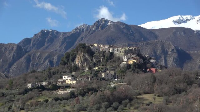 "The historic village of Castel San Vincenzo perched on a cliff with snow-capped Mainarde mountains in the background, Molise, Italy"
