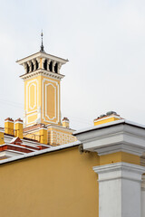 Elegant yellow tower with classical details and ornate spire rises above snowy rooftops, showcasing historic architecture, clean lines and soft pastel tones in a quiet urban winter scene