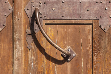 Weathered wooden door fragment with a curved metal handle, riveted iron hinges and rust patina, offering rich texture and aged character for architecture, restoration, design and historical projects