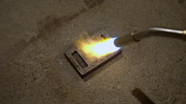 MAPP gas torch heats ingot mold in preparation for pouring molten metal.