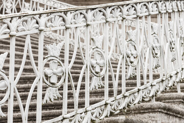 Ornate white wrought iron railing crowns weathered stone stairs, highlighting vintage decorative patterns, textured masonry, architectural details. Outdoor photo ideal for heritage and restoration