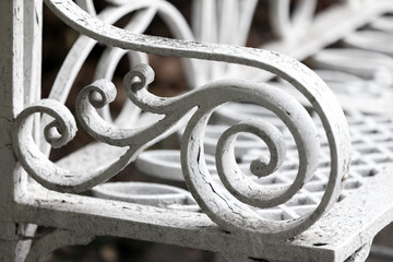 A detailed close-up of a decorative white wrought-iron railing featuring curling scrolls and cracked paint, conveying vintage charm, craftsmanship, and architectural elegance for decor and design