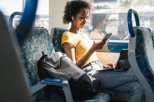Young woman with earphones using smartphone and tablet on a train