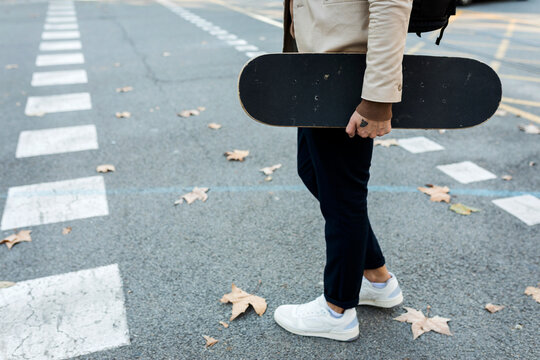 Man with backpack and skateboard crossing the street in autumn, partial view