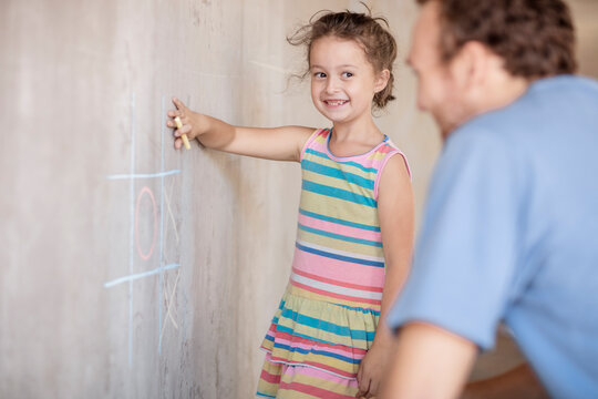 Father and daughter playing tic tac toe with chalk on a concrete wall