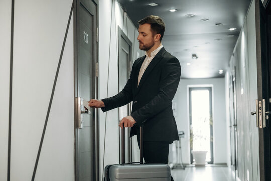 Businessman in a suit using a key card to unlock hotel room door while standing in a modern hotel corridor with stylish decor and bright lighting
