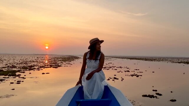 Red Lotus sea Thailand, Lake Nong Harn, where vibrant red lotus flowers bloom. A woman enjoys the view from her boat as the sun sets, creating a magical atmosphere in Udon Thani, Thailand.