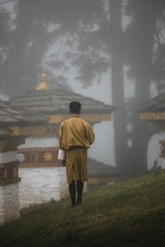 View of a lone figure in traditional attire walks amidst the ancient stupas shrouded in mist, creating an ethereal scene, Dochula Chorten, Thimphu, Bhutan.