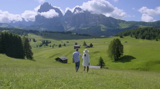 A couple strolls hand in hand through the lush green meadows of Seiser Alm, surrounded by magnificent Dolomite mountains Italy