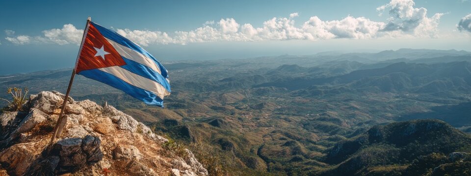 Cuban flag waving on a mountain peak with valleys and hills in the background under a clear blue sky