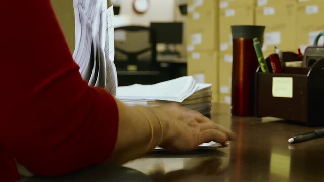 Close-up of a person's hands sorting through a large stack of documents on a desk