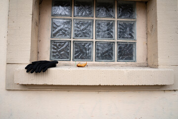 Black gloves on the left of a public bathroom window sill. Outdoor urban scene showing everyday personal objects.