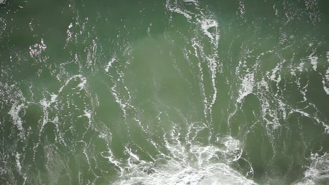 Ocean wave breaking green sea water crashes and creates white foam in a powerful overhead shot of the rhythmic tide