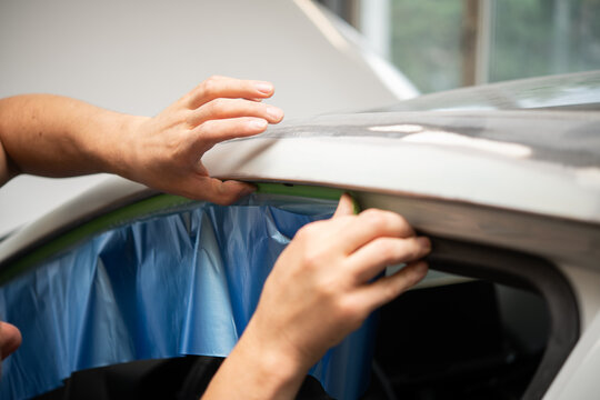 Closeup of hands masking car window in auto body shop