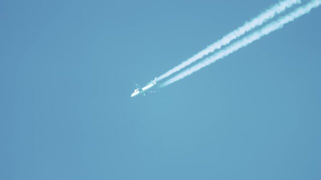 Passenger aircraft flying at high altitude leaving exhaust trails across blue sky. Jet engines releasing harmful emissions contributing to environmental pollution and harming ecology. Aviation sector
