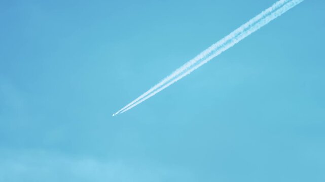 Commercial airplane flying across clear sky leaving long exhaust trails. Jet engines emitting harmful emissions increasing environmental pollution and affecting global ecology. Air transport
