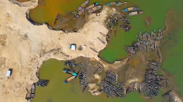 Aerial view of numerous boats clustered around the riverbank, contrasting the sandy shores with the green waters, Sunamganj, Sylhet Division, Bangladesh.