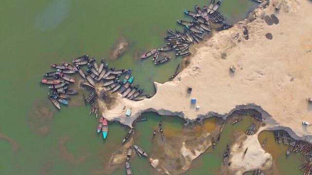 Aerial view of numerous boats clustered along the sandy riverbank where the muddy river meets the shore, creating a stunning contrast, Sunamganj, Bangladesh.