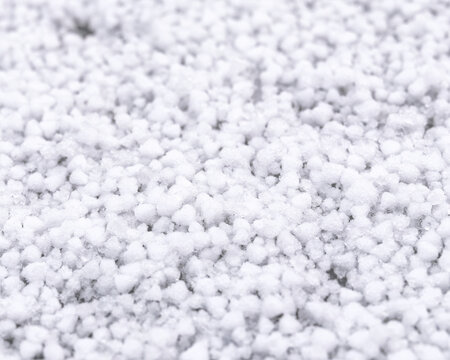 Macro photography of white graupel ice pellets covering the ground in winter. Close up detail of soft hail texture with soft bokeh.