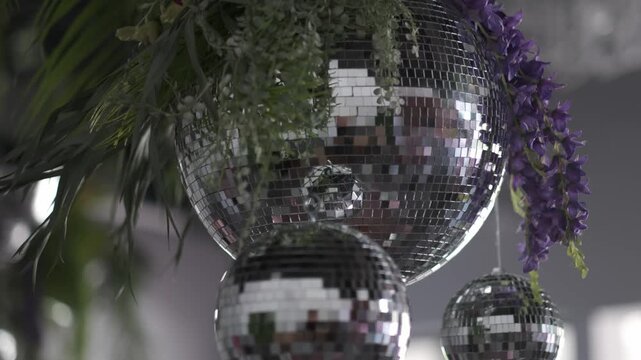 Close up of sparkling disco balls hanging with purple flowers and green plants. Zoom in.