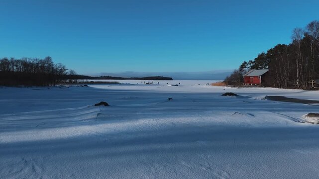 Aerial view of a snow-covered landscape and a red cabin, the stark white contrasting with the dark trees, Rukajoenranta, Satakunta, Finland.
