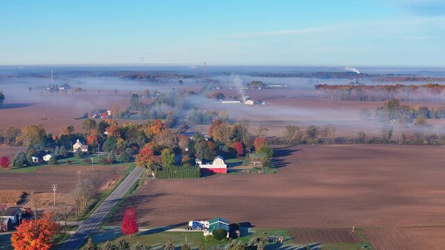 Lake Odessa, Michigan, USA with autumn fog over farmland inwide aerial view, Autumn colors appearing on trees, farms and homes nestled in early morning fog