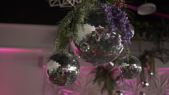 Sparkling disco balls decorated with purple wisteria and tropical greenery hanging in a club
