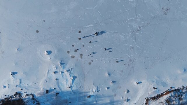 Aerial view of a snowy frozen lake speckled with dark spots and shadows of people enjoying the winter landscape, Rukajoenranta, Satakunta, Finland.