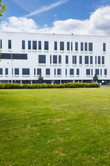 Modern white building with large windows and green lawn in front, under a blue sky with clouds, showcasing contemporary architectural design and landscaping