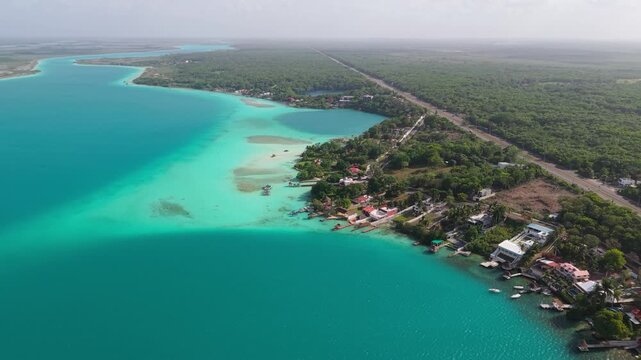 Aerial view of the turquoise waters meeting the lush green coastline, creating a striking contrast of colors and textures, Bacalar, Quintana Roo, Mexico.