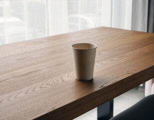 White paper cup mockup on a wooden table in a bright interior
