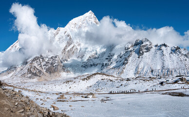 Line of hikers with trekking poles can be making their way along rocky trail towards village of Gorakshep, last stop before Everest Base Camp with view of snow-capped Himalayan peaks