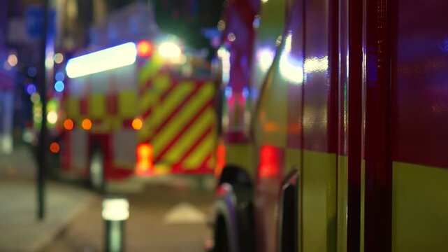 Nighttime emergency lights flashing fire truck parked along residential city street during urgent response. Reflective panels glowing on firefighting vehicles standing close together in urban