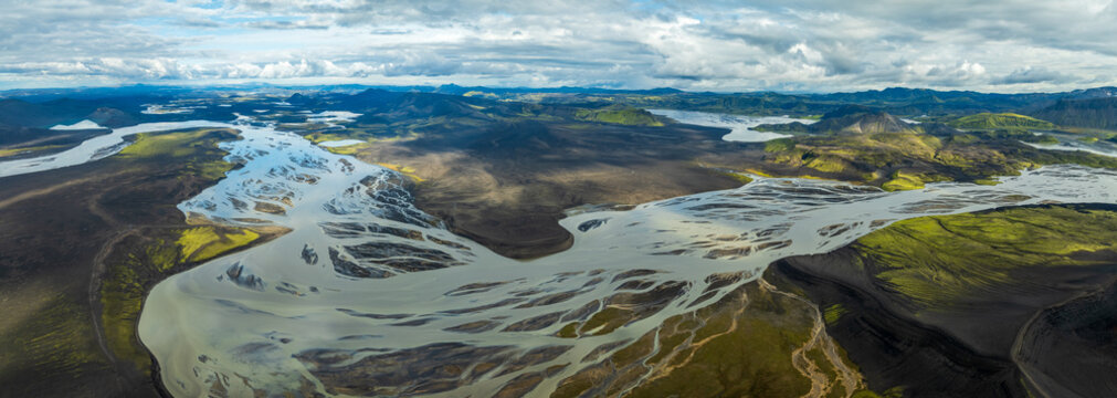 Aerial view of glacial rivers carving through stark volcanic landscapes and verdant moss fields under a dramatic sky, Hnausapollur, Rangarthing ytra, Iceland.