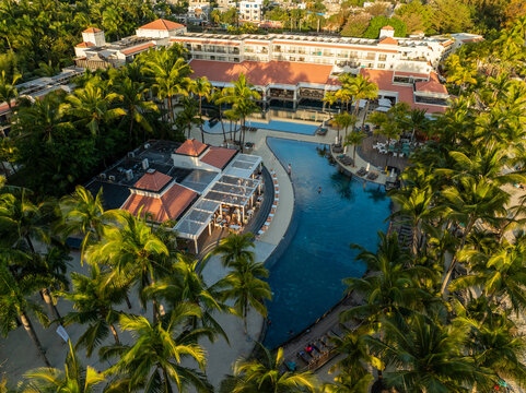 Aerial view of a vibrant resort with a winding pool reflecting the sky, nestled among dense palm trees under the warm sun, Grand Baie, Riviere du Rempart District, Mauritius.