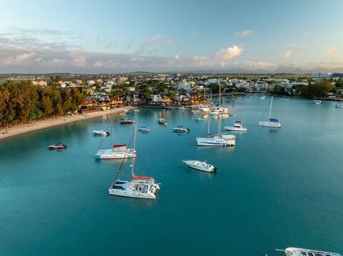 Aerial view of boats gently bobbing in the turquoise bay waters near the coastline dotted with buildings and trees, Grand Baie, Riviere du Rempart District, Mauritius.