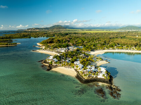 Aerial view of turquoise waters meeting sandy shores, dotted with buildings and lush greenery, Shangri La, Trou d'Eau Douce, Mauritius.