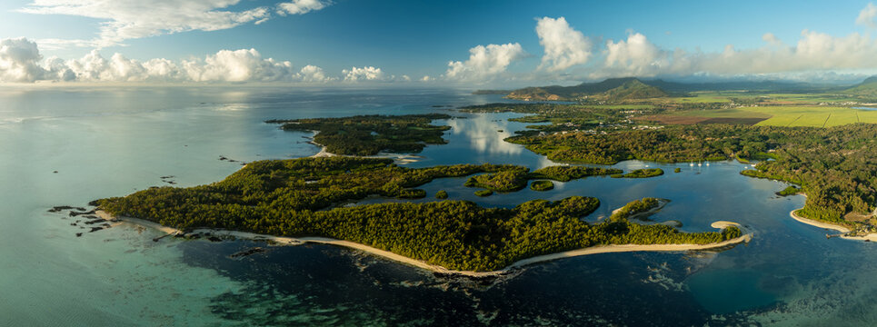 Aerial view of lush green islands fringed with white sand beaches meeting the turquoise sea under a blue sky dotted with fluffy clouds, Shangri La, Trou d'Eau Douce, Mauritius.