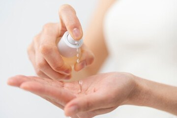 スキンケアプロセス。ポンプ式容器、美容液、化粧水を手元に出している女性の手元。