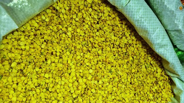 A high-angle, close-up shot of a large sack filled with yellow split peas (Chana Dal) at a market.
The video captures the vibrant yellow color and uniform texture of the dried legumes in bulk.