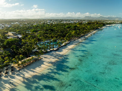 Aerial view of the coastline where the turquoise sea meets the white sandy beach near the lush greenery of palm trees, Triolet, Pamplemousses, Mauritius.