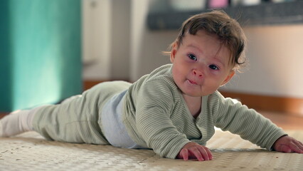 Naklejka premium Baby smiling and lifting body while lying on a mat, engaging in early development, showing happiness and curiosity during tummy time in a cozy indoor environment