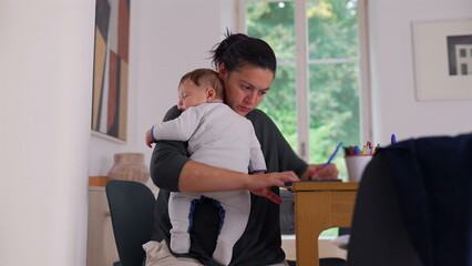 Fototapeta premium Mother holding her baby while using a smartphone and writing at a desk, balancing childcare with work, focused on completing tasks in a calm and nurturing home office