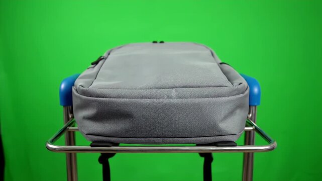 A gray backpack on a stainless steel cart in front of a green screen background. studio shot