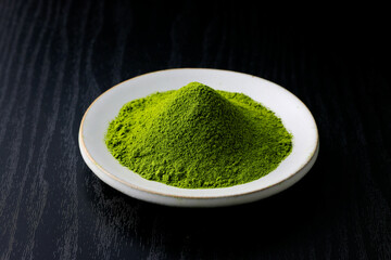 黒背景の木目に映える鮮やかな日本の抹茶の粉末　Vibrant Japanese matcha green tea powder on dark wood background