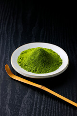 黒背景の木目に映える鮮やかな日本の抹茶の粉末　Vibrant Japanese matcha green tea powder on dark wood background