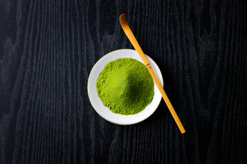 黒背景の木目に映える鮮やかな日本の抹茶の粉末　Vibrant Japanese matcha green tea powder on dark wood background